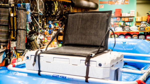 Front view of a padded black mesh chair strapped down to a rafting cooler with cam straps on a blue Hyside raft. 
