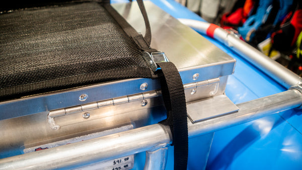 The cam strap attachment point of a padded river chair strapped to a dry box.