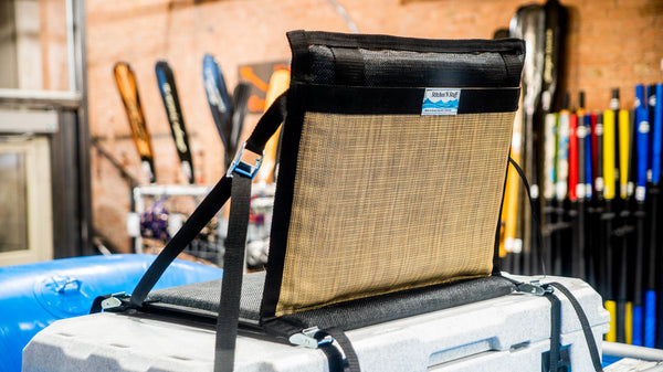 A padded tan and black chair strapped down to a rafting cooler with cam straps.