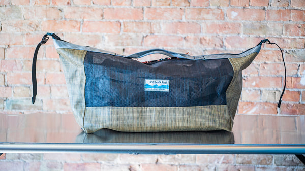 A tan and black mesh duffle bag showing the middle carry handle and the side clip unclipped to show the size versatility of the bag. 