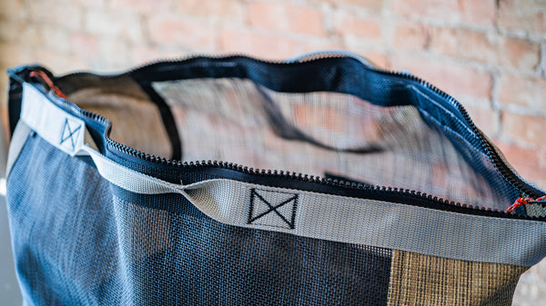 A tan and black mesh duffle bag with the zipper opened to show how wide the top opens. 