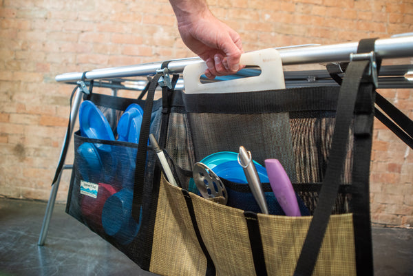 A tan and black mesh dish dryer displaying utensils drying and attached to a raft table. 