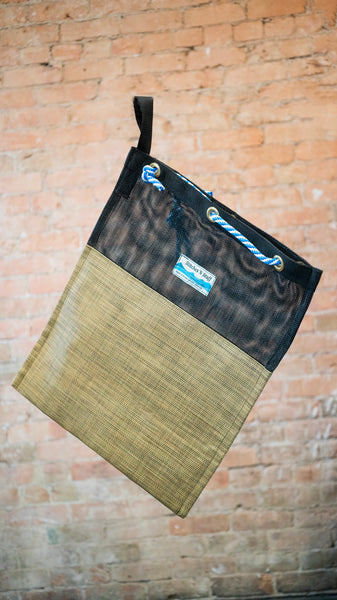 A black and tan mesh drag bag for river use showing the rope cinch closure and webbing carry handle.