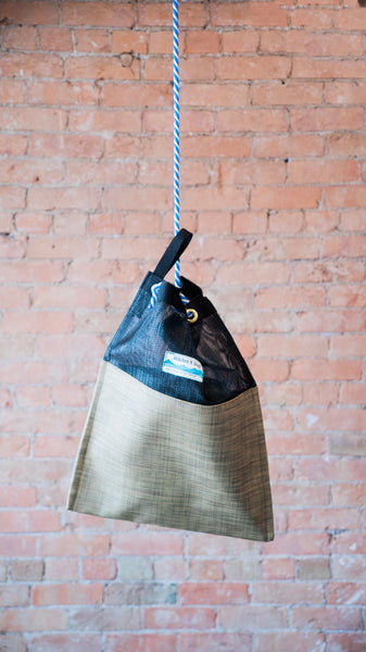 A black and tan mesh drag bag for river use showing the rope cinch closure and webbing carry handle.