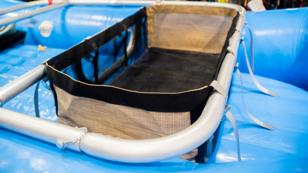 A black mesh drop bag with heavy-duty  Tan side panels, designed for rigging gear on a raft, displayed on a blue Hyside raft.