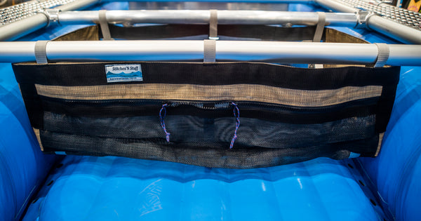 A Black and tan mesh drop bag with a zippered pocket in the front attached to a raft frame on a blue Hyside boat. 