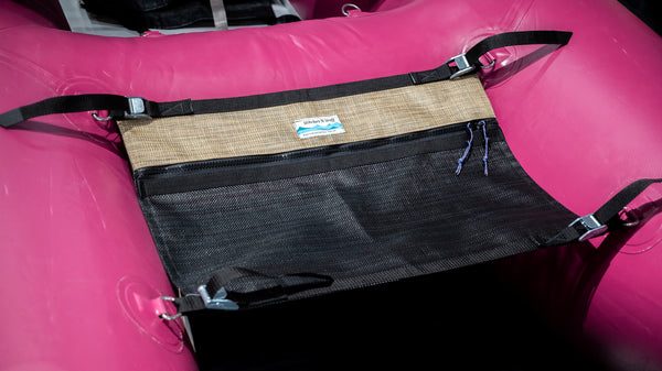 A black and tan mesh storage bag for a cataraft attached to a pink cataraft. 