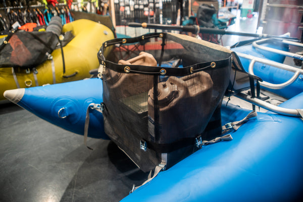 Tan and black mesh bag strapped with grey webbing to a blue cataraft showing the lid opened and the contents that it can hold including rocket boxes and water jugs. 