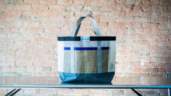 A multi colored mesh tote showing carry handles  and front exterior pocket shown on a river table. 