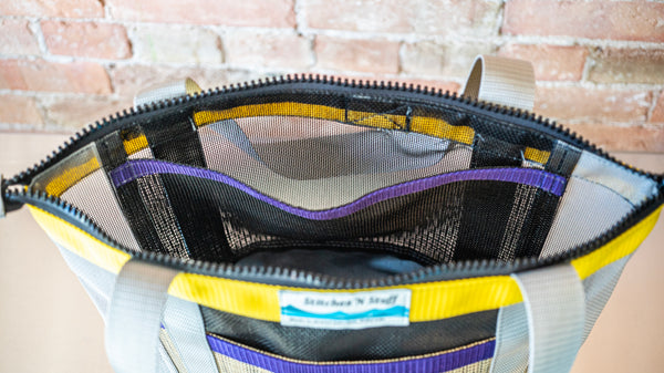 Tan and grey mesh zipper top tote with multi colored webbing showing the zippered opening and internal pockets.  