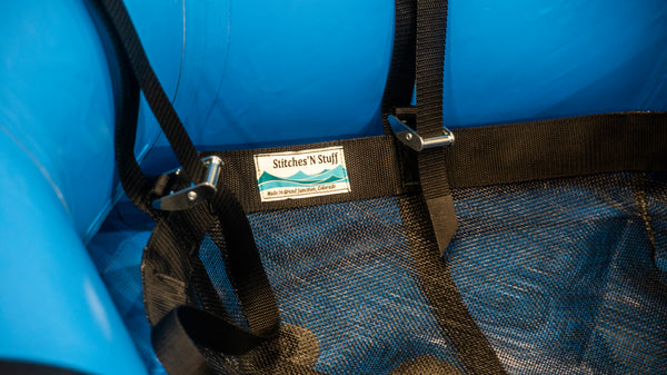 Close up of black mesh cargo floor displayed in blue raft with straps attached to raft and raft frame. 