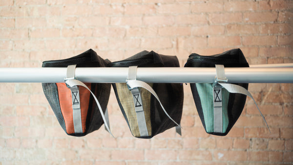 Side view of the three colors of the Every Square Inch Storage bag and its cam buckle attachments to a raft frame. 