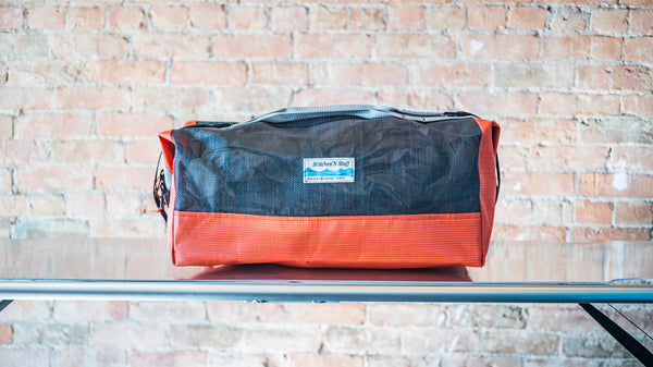 An orange and black mesh duffle bag showing carry handles, side closures all on a river table. 