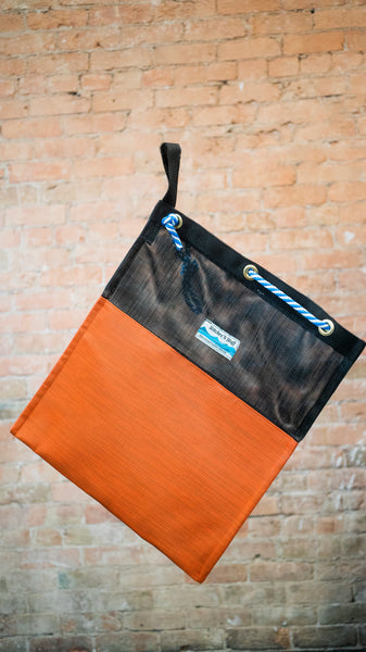 A black and orange mesh drag bag for river use showing the rope cinch closure and webbing carry handle.
