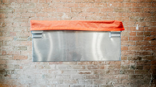 Padded orange mesh cover with orange webbing sitting on top of an aluminum dry box.