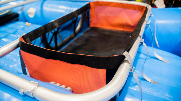 A black mesh drop bag with heavy-duty  orange side panels, designed for rigging gear on a raft, displayed on a blue Hyside raft.