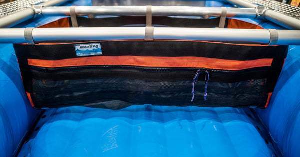 A Black and orange mesh drop bag with a zippered pocket in the front attached to a raft frame on a blue Hyside boat. 