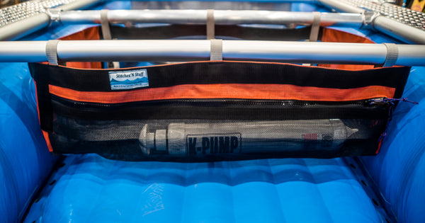 A Black and orange mesh drop bag with a zippered pocket in the front attached to a raft frame on a blue Hyside boat. Contents of the zippered pocket are a raft pump