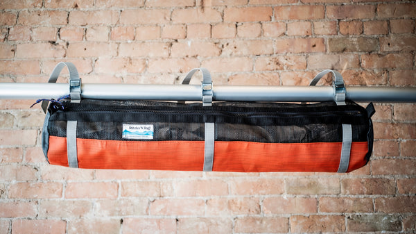 Orange and black mesh raft frame storage bag with full length zipper and three cam buckle attachments for securing to raft frame. 
