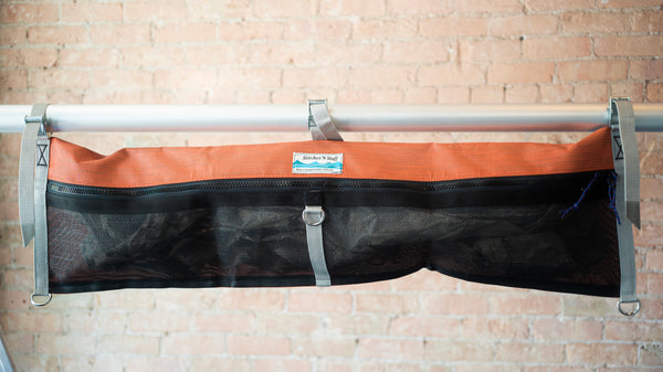Orange and black mesh raft frame storage bag with full length zipper and three cam buckle attachments for securing to raft frame. 
