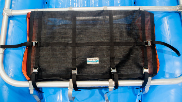 A top view of an orange and black mesh drop bag with a lid shown strapped to a raft frame on a blue raft. 