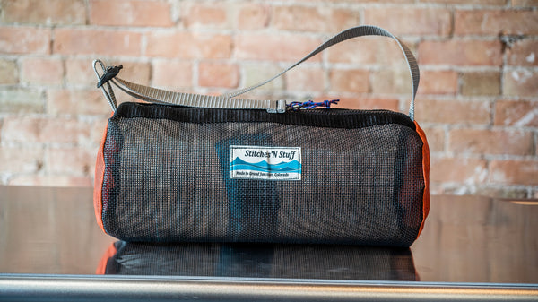 An orange and black cylindrical mesh duffle bag showing the zipper and carry handle on a raft table. 