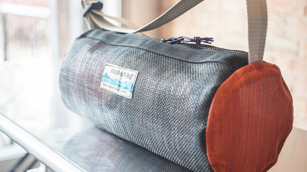 An orange and black cylindrical mesh duffle bag showing the zipper and carry handle on a raft table. 