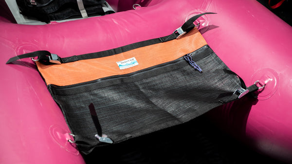 A black and orange mesh storage bag for a cataraft attached to a pink cataraft. 
