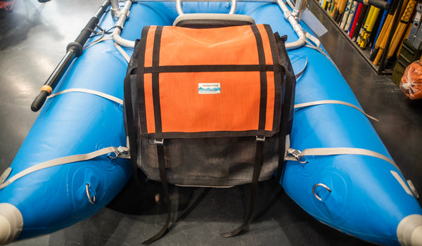 Orange and black mesh bag strapped with grey webbing to a blue cataraft. 