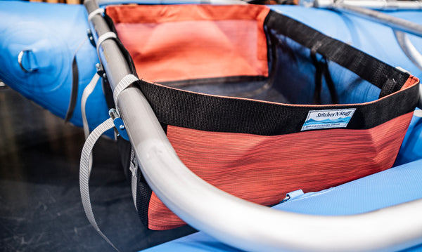 A black drop bag with orange heavy duty sides attached to a blue Rocky Mountain Rafts raft.