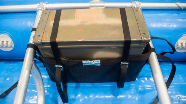 A black mesh sling holding a rocket box attached to a raft frame on a blue raft. 