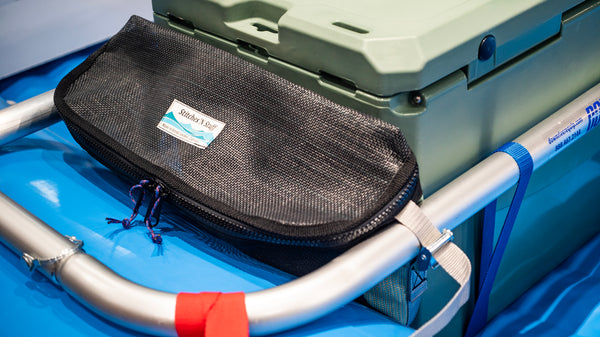 Black and green mesh bag sitting on a blue Hyside raft attached to the raft frame next to a cooler. 