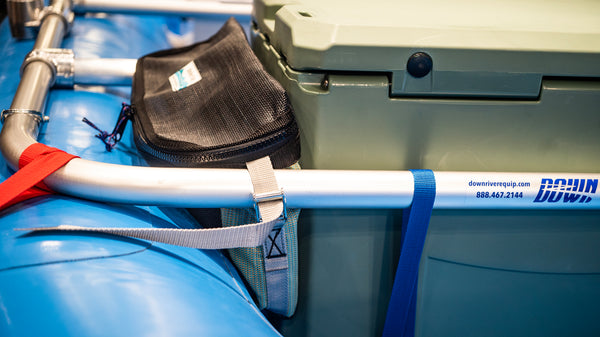 Side view of a green and black mesh bag showing the triangular profile to sit between the blue Hyside raft tube and the cooler. 