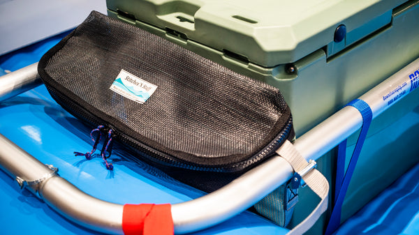 Black and green mesh bag sitting on a blue Hyside raft attached to the raft frame next to a cooler. 