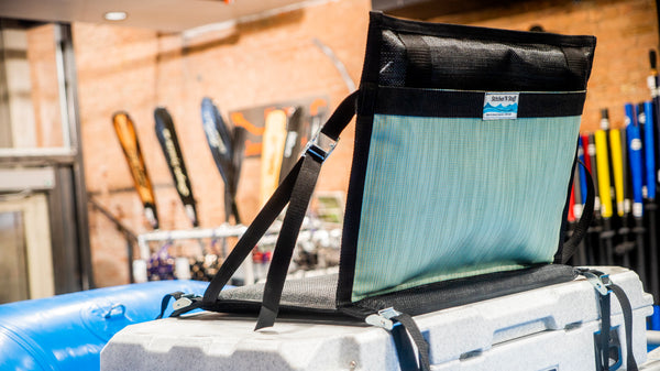 A padded green and black chair strapped down to a rafting cooler with cam straps.