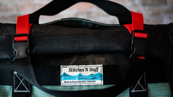 Black and green mesh bag showing the Stitches N Stuff branded label and buckles to secure the lid closed. 
