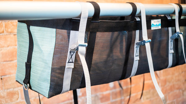 A green and black mesh bag with two rocket boxes intended for rafting strapped to the bag attached to a raft frame. 