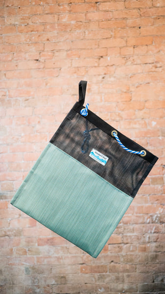 A black and green mesh drag bag for river use showing the rope cinch closure and webbing carry handle.