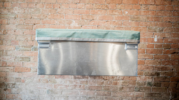 Padded green mesh cover with grey webbing sitting on top of an aluminum dry box.