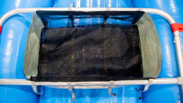 A black mesh drop bag with heavy-duty  green side panels, designed for rigging gear on a raft, displayed on a blue Hyside raft.