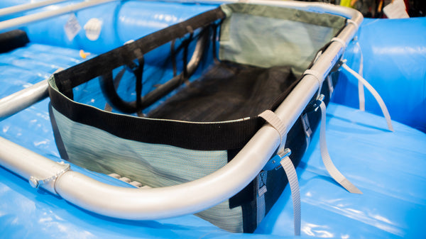 A black mesh drop bag with heavy-duty  green side panels, designed for rigging gear on a raft, displayed on a blue Hyside raft.