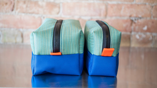 Two green rectangular storage bags with blue bottoms showing the size difference between the small and large from the side on a river table