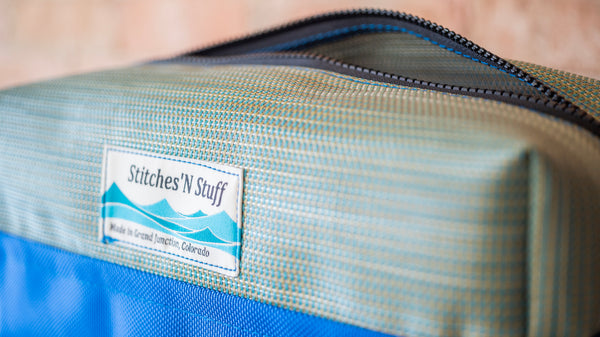 A side view of a green rectangular storage bag with the zipper open and the Stitches N Stuff branded label visible.