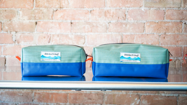 Two green rectangular storage bags with blue bottoms showing the size difference between the small and large size on a river table. 