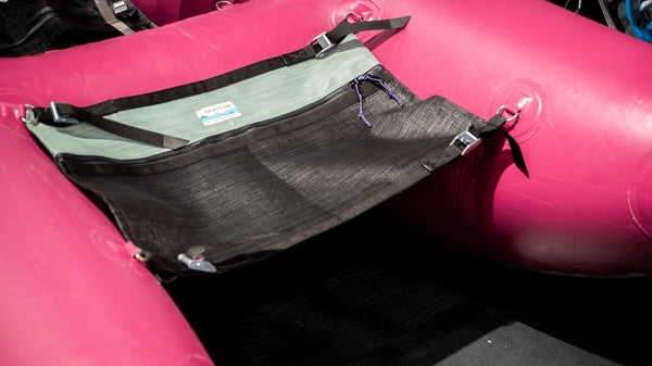 A black and green mesh storage bag for a cataraft attached to a pink cataraft. 