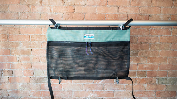 Green and black mesh storage bag for use rafting displayed on a raft frame