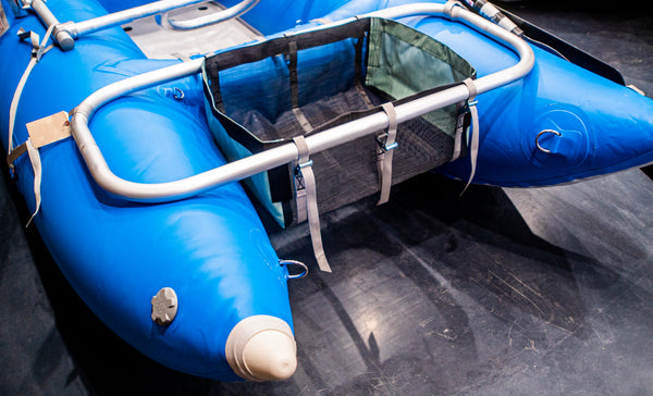 A black drop bag with green heavy duty sides attached to a blue Rocky Mountain Rafts raft.