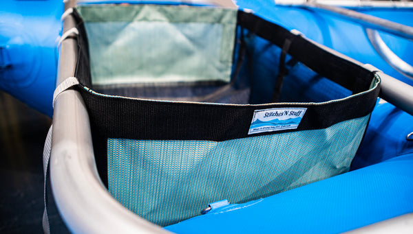 A black drop bag with green heavy duty sides attached to a blue Rocky Mountain Rafts raft.